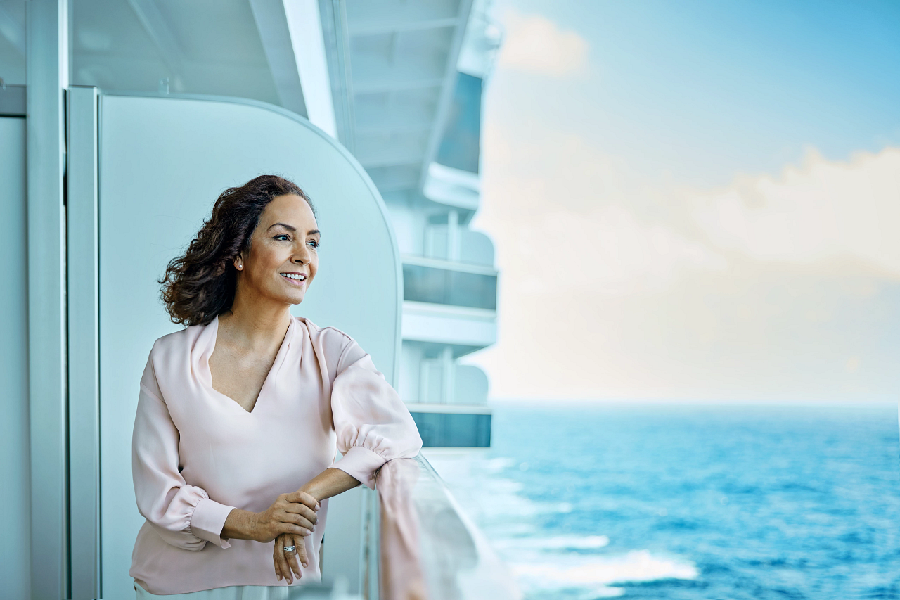Kvinne ser utover havet fra balkongen på et cruiseskip.