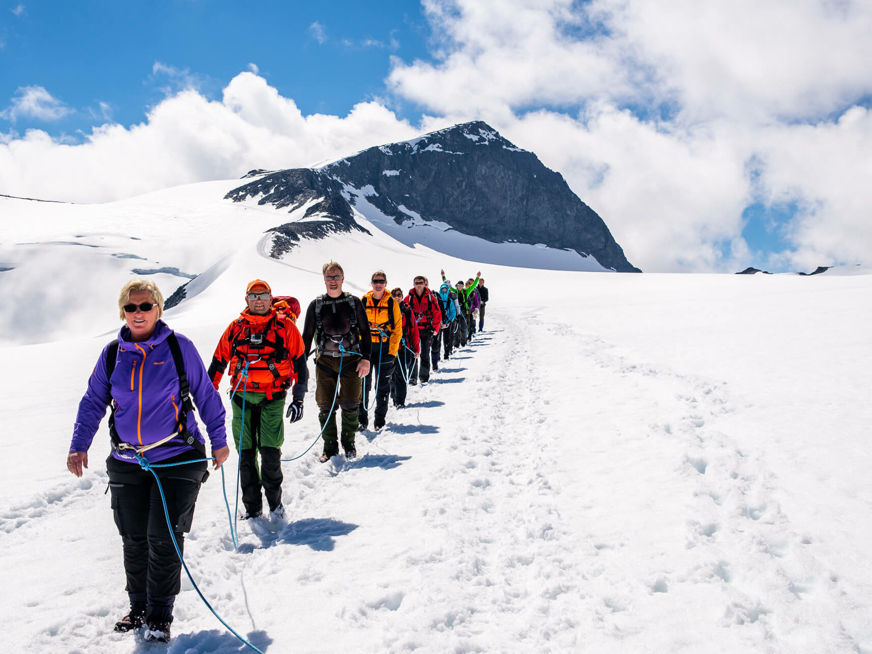 Mennesker går i taulag over snø på vei ned fra fjelltopp. Foto