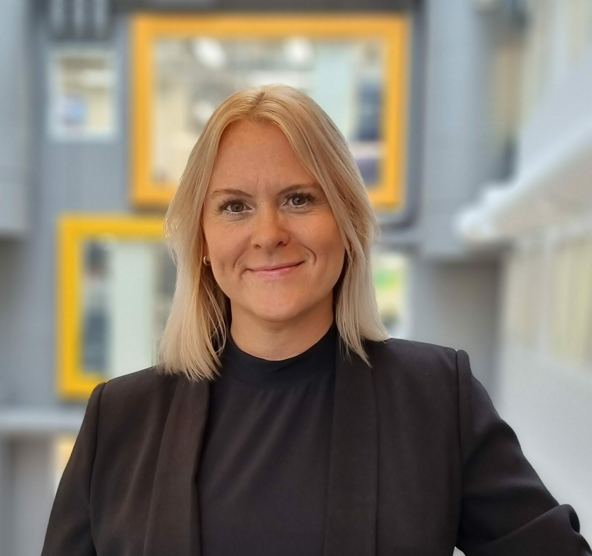 Kvinne i kontorlandskap smiler inn i kamera. Foto
