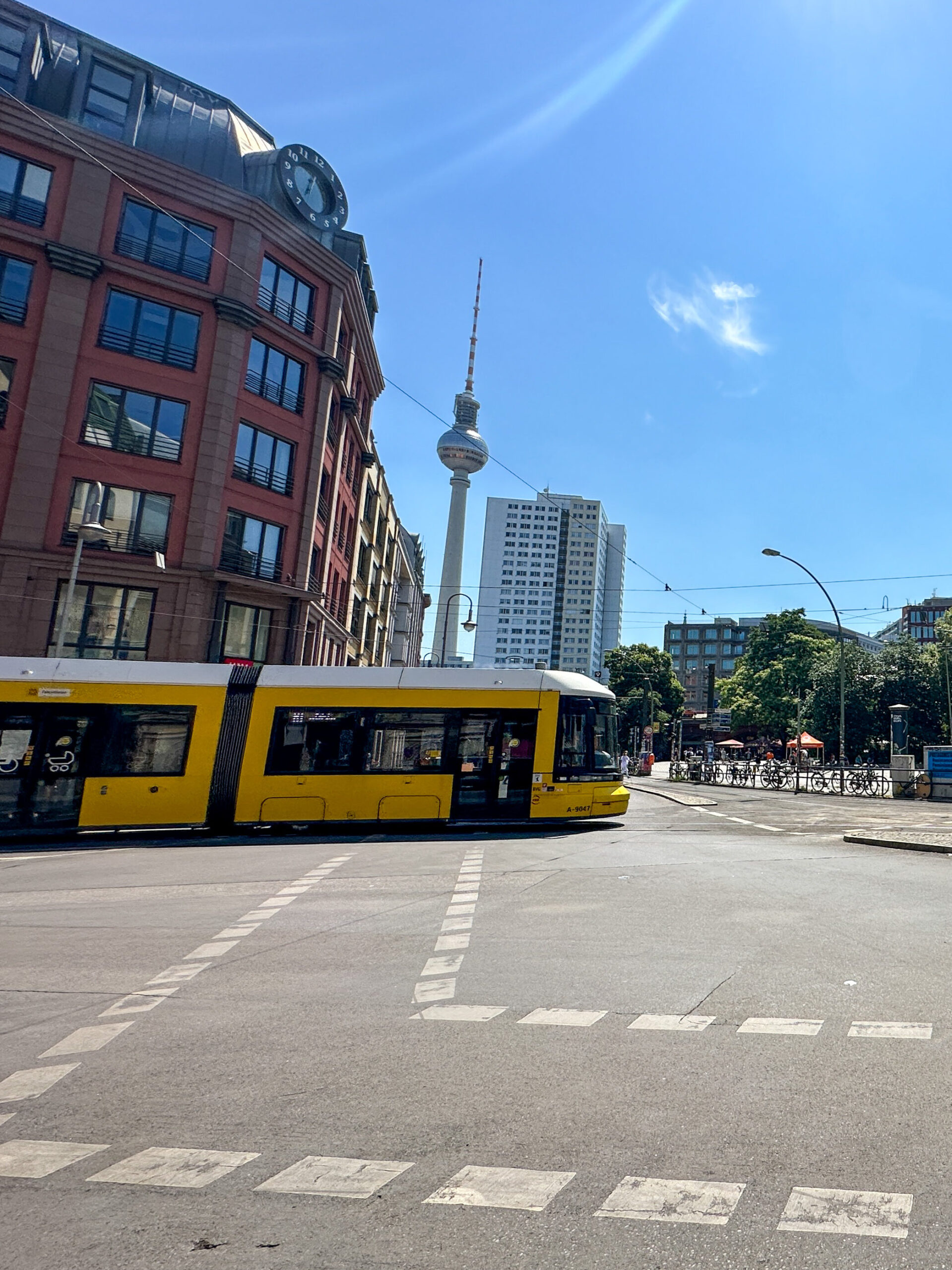 En gul trikk som kjører over et veikryss i Berlin med TV-tårn i bakgrunnen. Foto