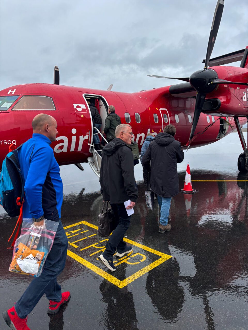 Tre personer foran et rødt propellfly. Foto
