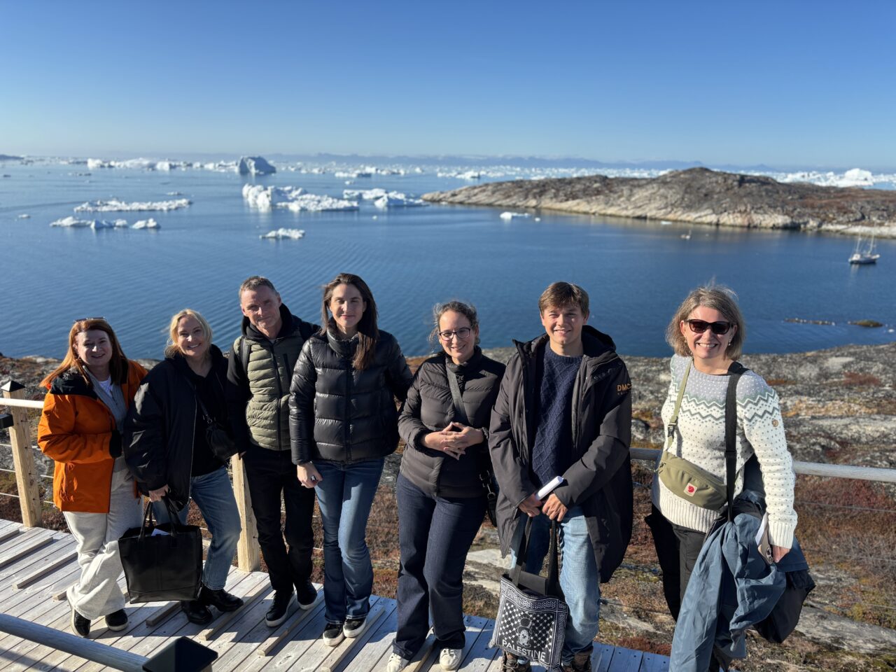 Syv personer står sammen foran en fjord. Foto