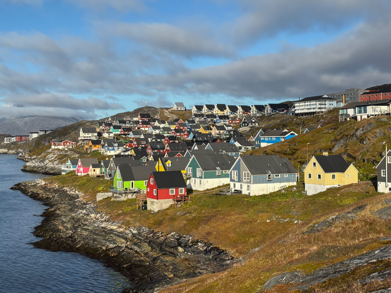 Fargede hus på nedsiden av et fjell mot havet. Foto