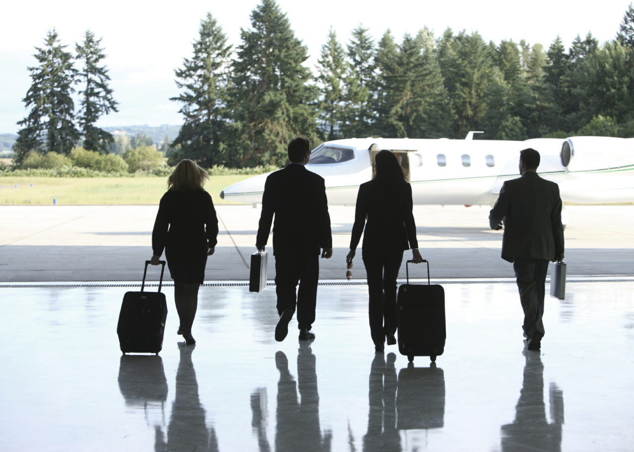 Liten gruppe forretningsreisende går mot et privat jetfly med trillekofferter