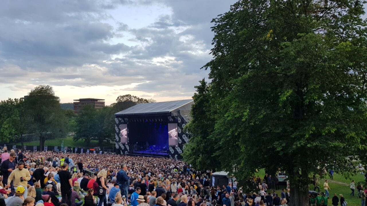 Et hav av mennesker sitter foran en stor scene i en park. Foto