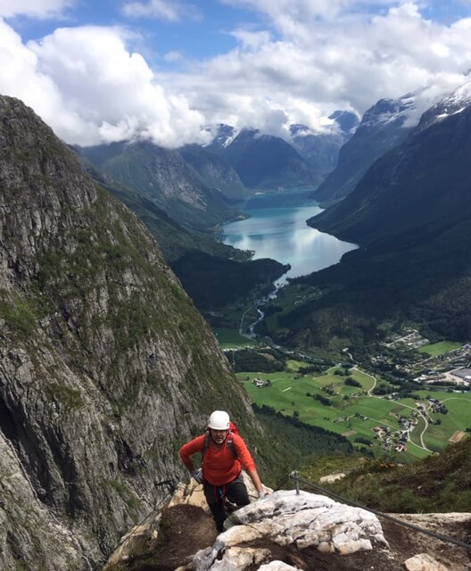 Mann på vei opp fjellet med utsikt over Loen bak seg