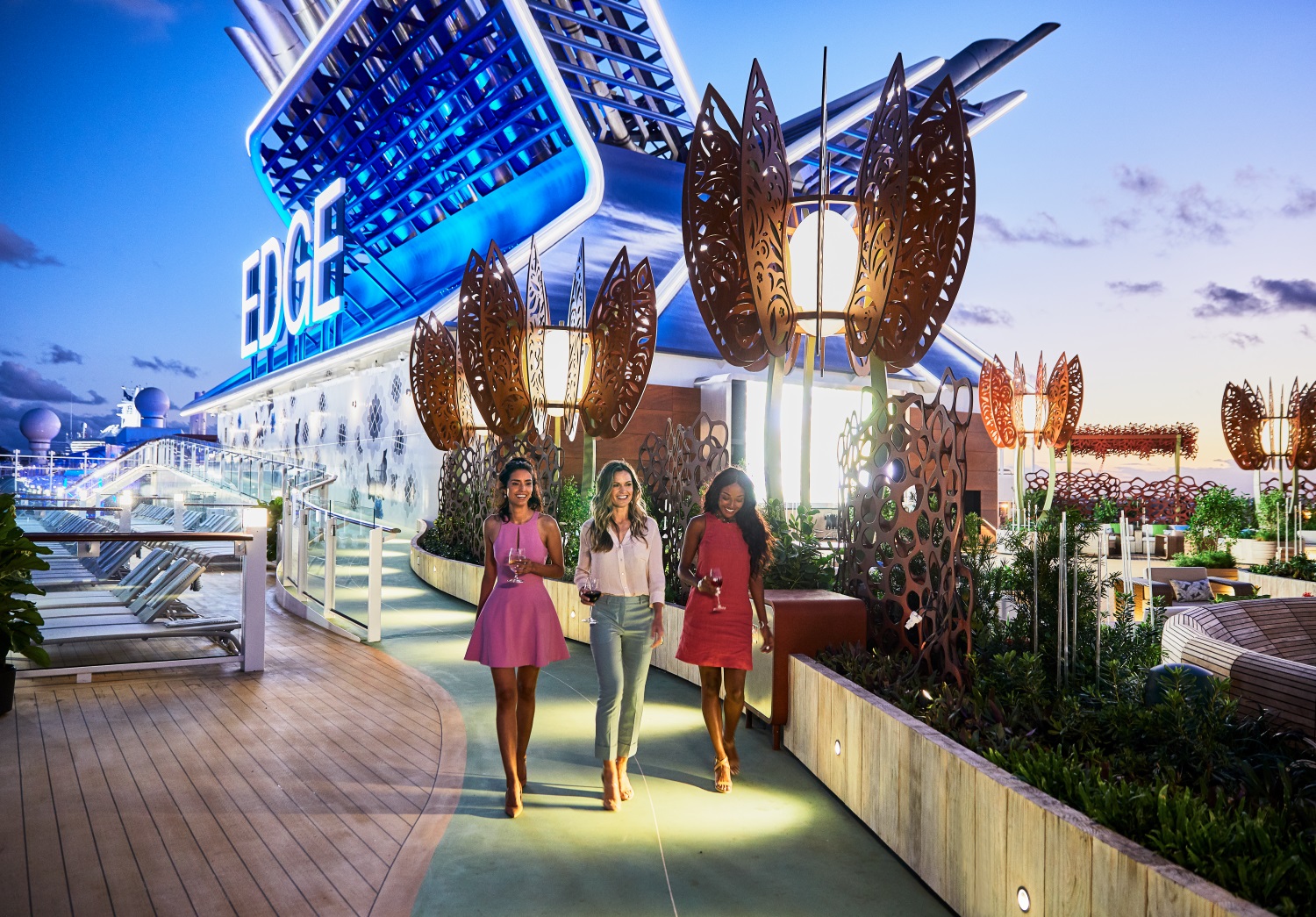 Tre ungdomsjenter går tur på dekk mellom planer og solsenger, om bord cruiseskipet Celebrity Edge