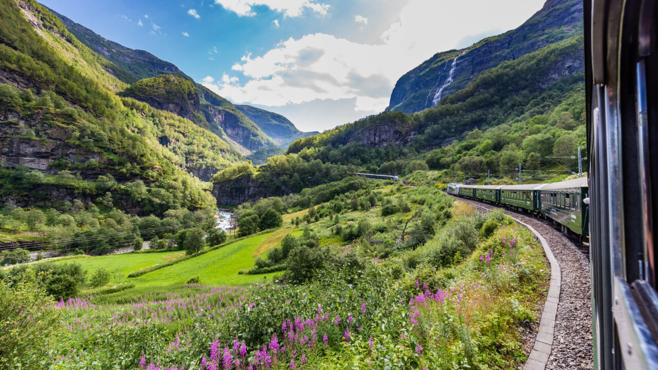 Grønt tog kjører opp gjennom en frodig dal på vei til Flåm