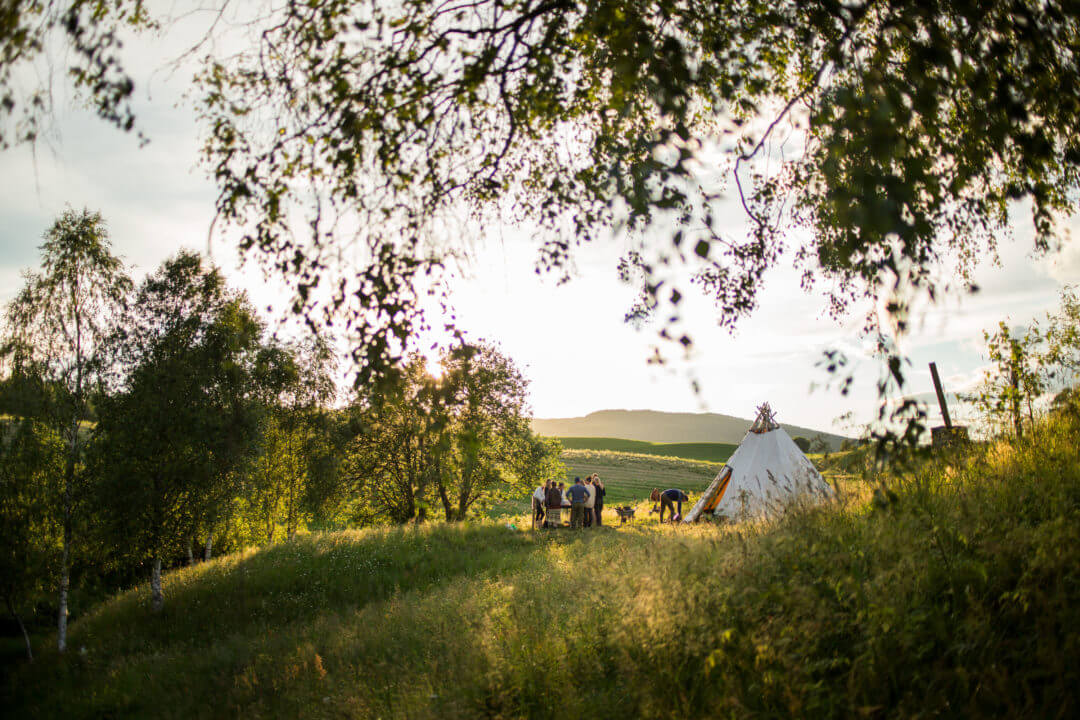 Sommereng med folk samlet rundt en lavvo