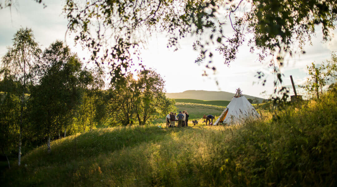 Sommereng med folk samlet rundt en lavvo