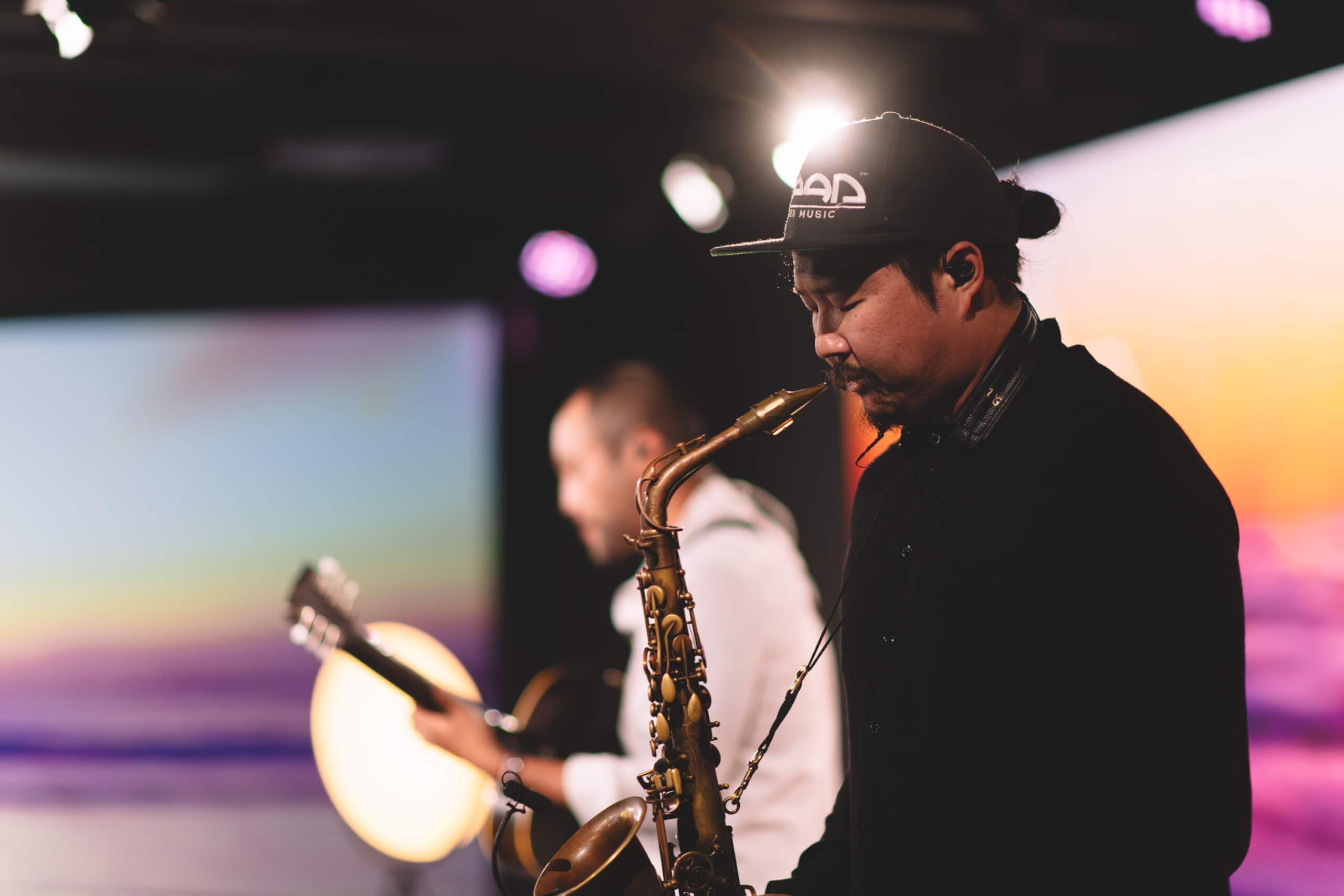 En saksofonist og en gitarist står på scenen og spiller under et digitalt arrangement