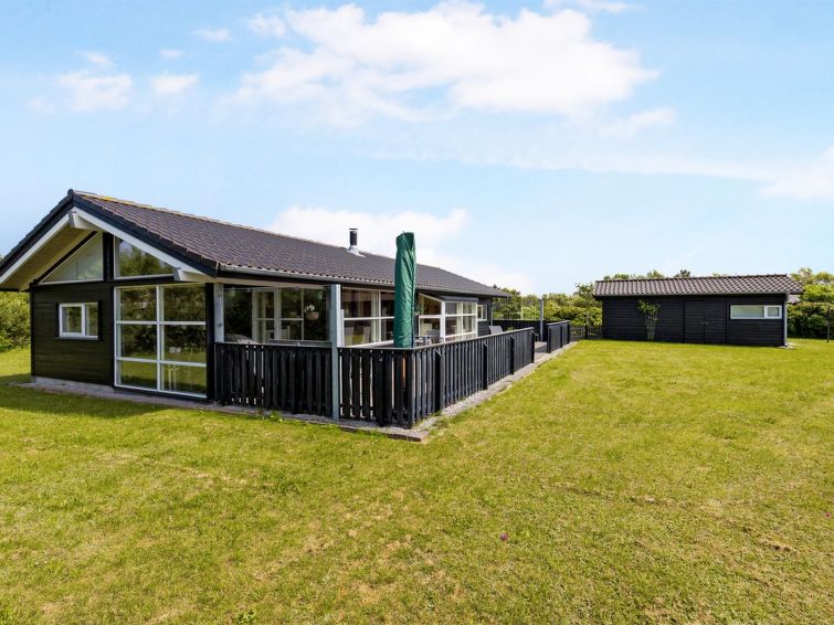Hus i mørk tre over ett plan, omringet av stor grønn gressplen. Foto