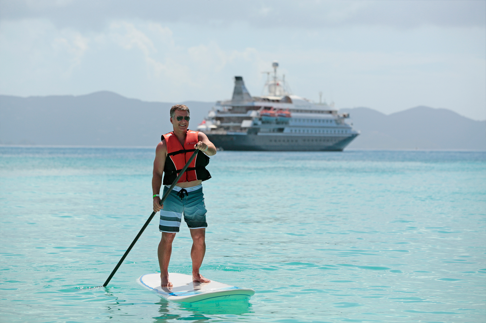 Mann med redningsvest står på et paddleboard foran et cruiseskip fra SeaDream