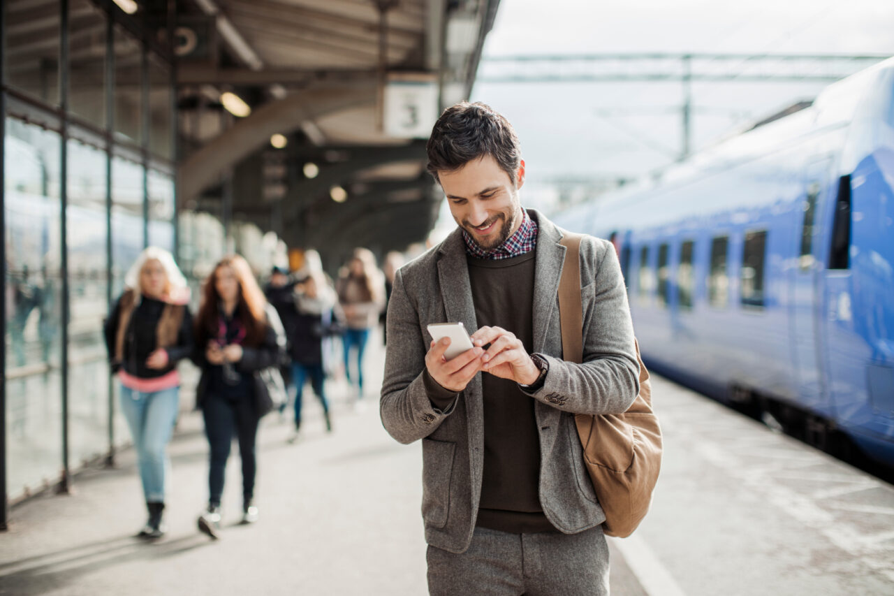 Forretningsmann ser på mobilen i det han går ut av toget. Foto