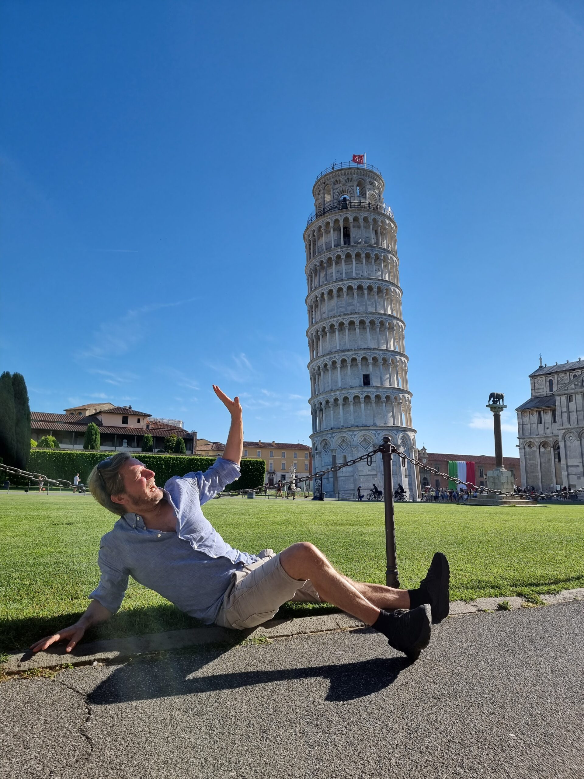 Mann sitter på bakken og leker som han får det skjeve tårnet i Pisa over seg