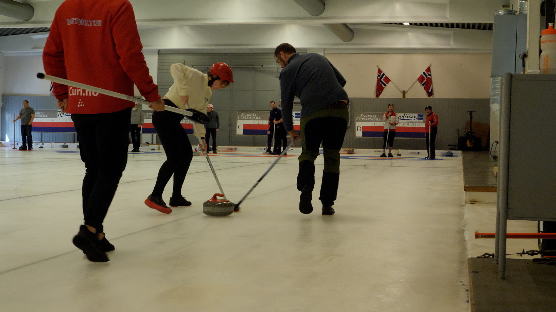 Deltakere står ute på isen og spiller curling