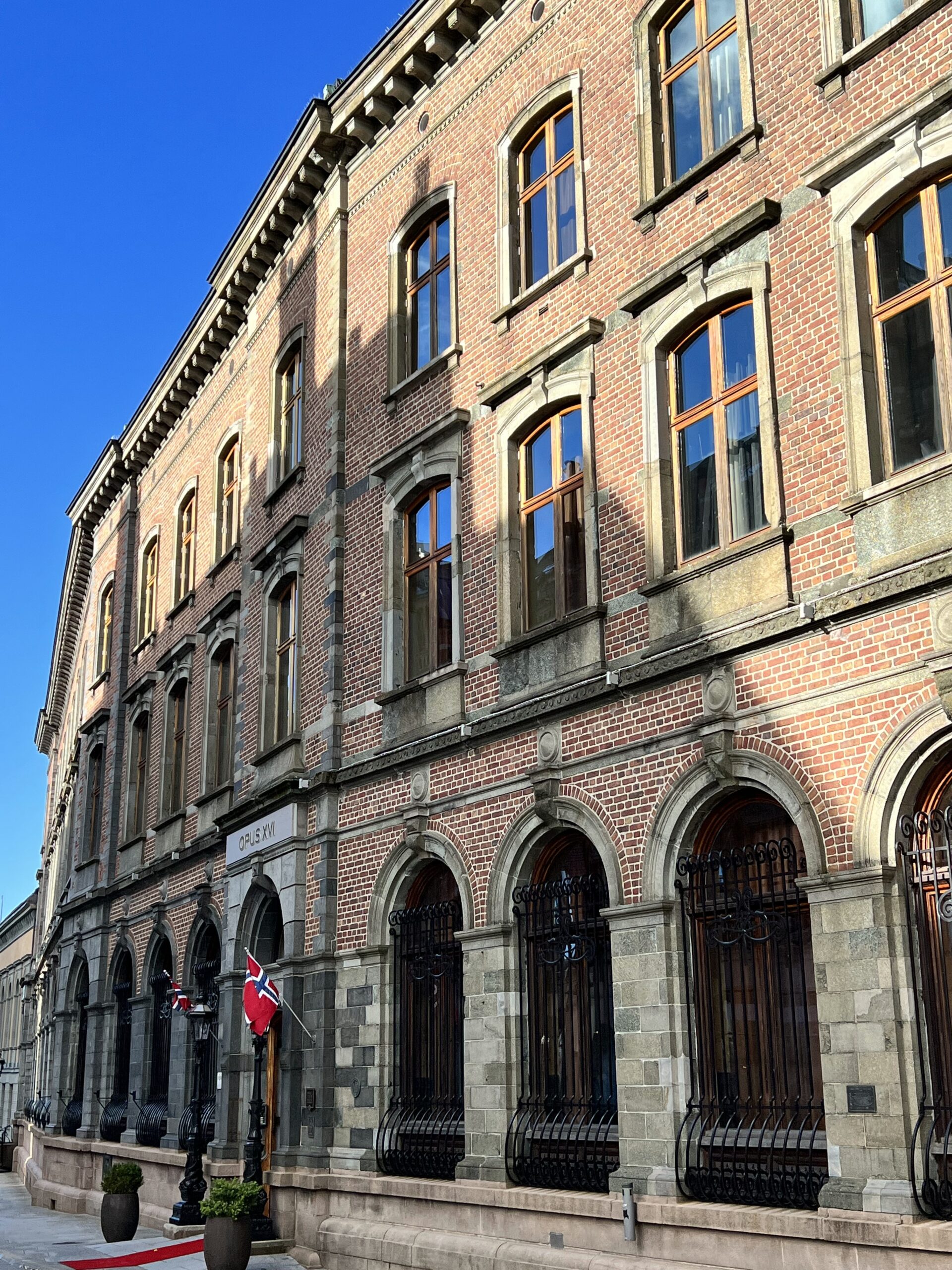 Gammel mursteinsbygning med rød løpet og norske flagg