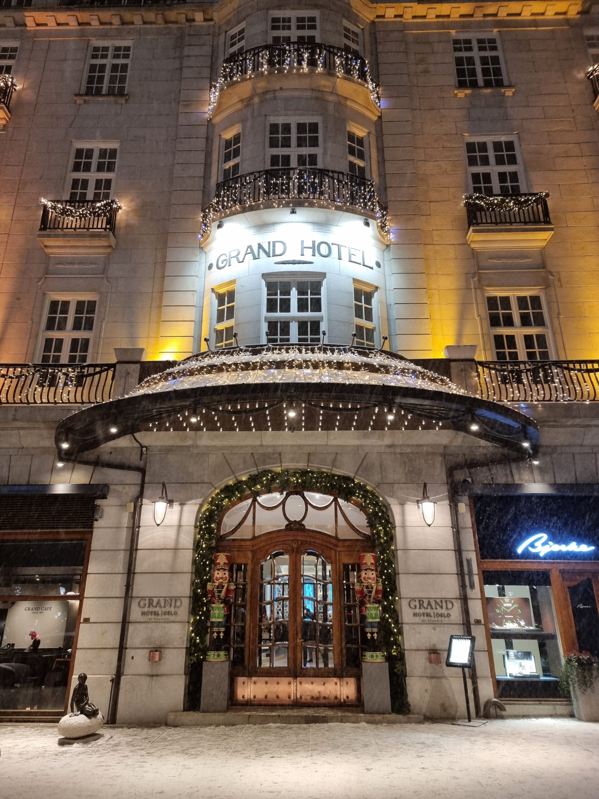Inngangen til et hotell med stor tredør, nøtteknekkere på hver side av døren, og masse julelys. Foto