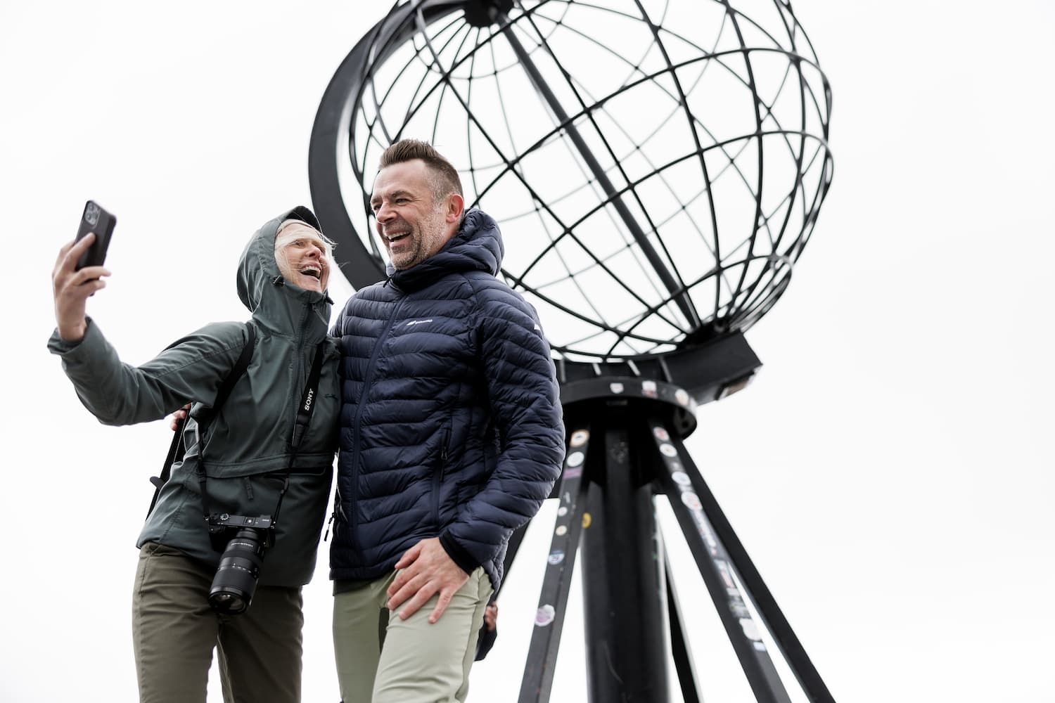 En mann og en kvinne står foran et monument som forteller at du er på Nordkapp. Foto