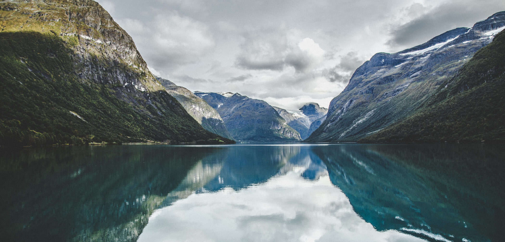 Klart vann og fjelltopper som skyter opp av fjorden. Foto