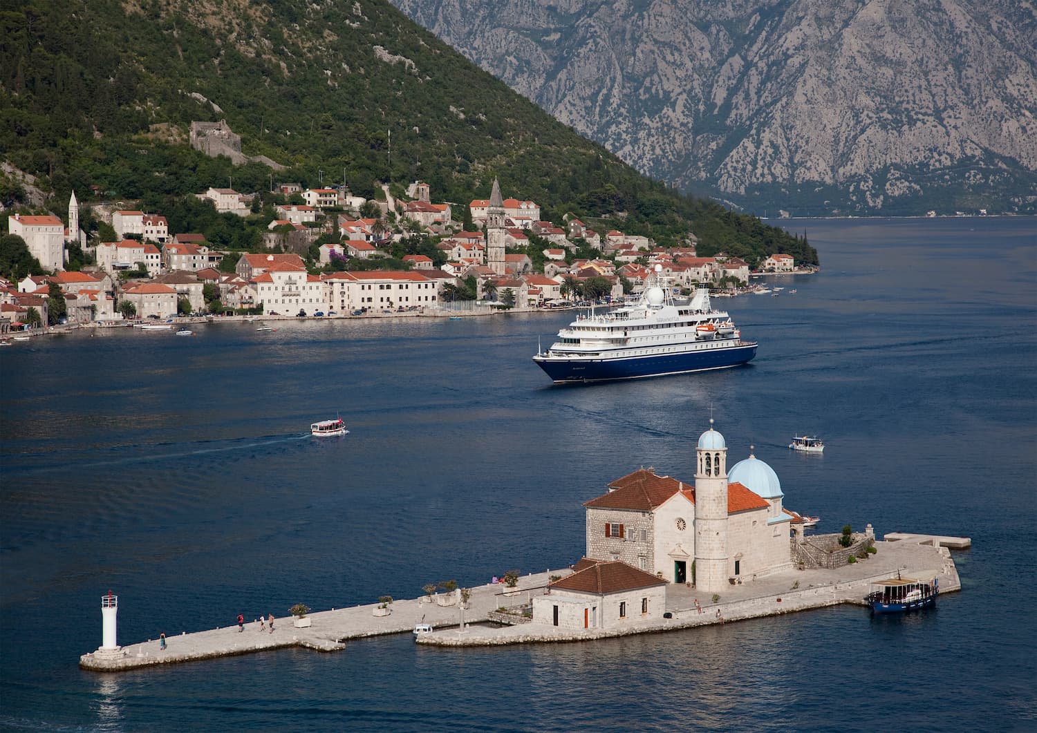 En lite cruiseskip seiler inn til en havn mellom gamle mursteinsbygninger. Foto