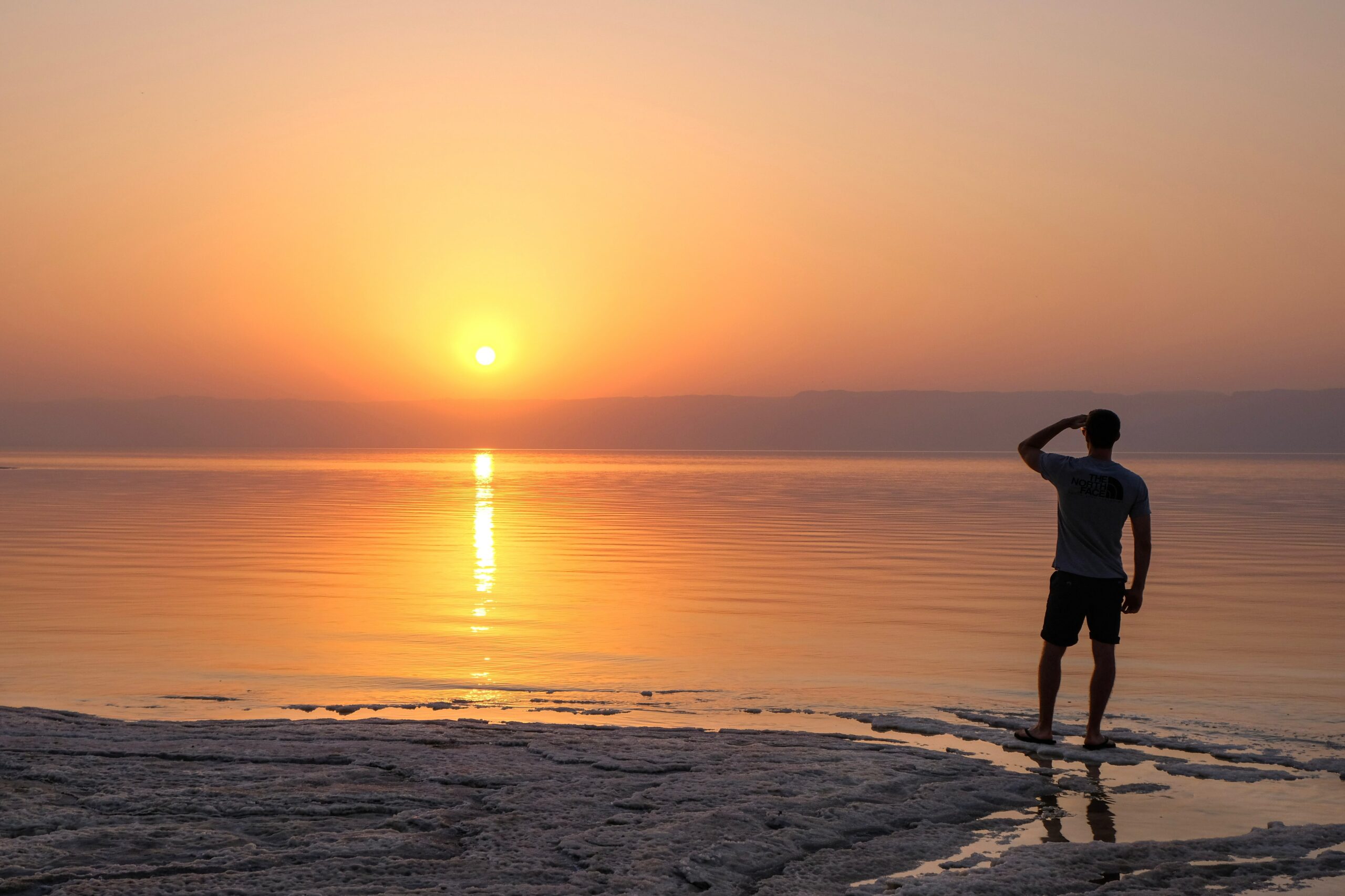 Person står med ryggen til og ser ut over havet i solnedgang. Foto