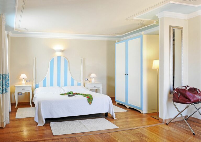 Hotel Palazzo Sa Pischedda - lyst rom med dobbeltseng. Stipete sengegavel med blått og hvitt. Matchende klesskap. Foto WebBeds