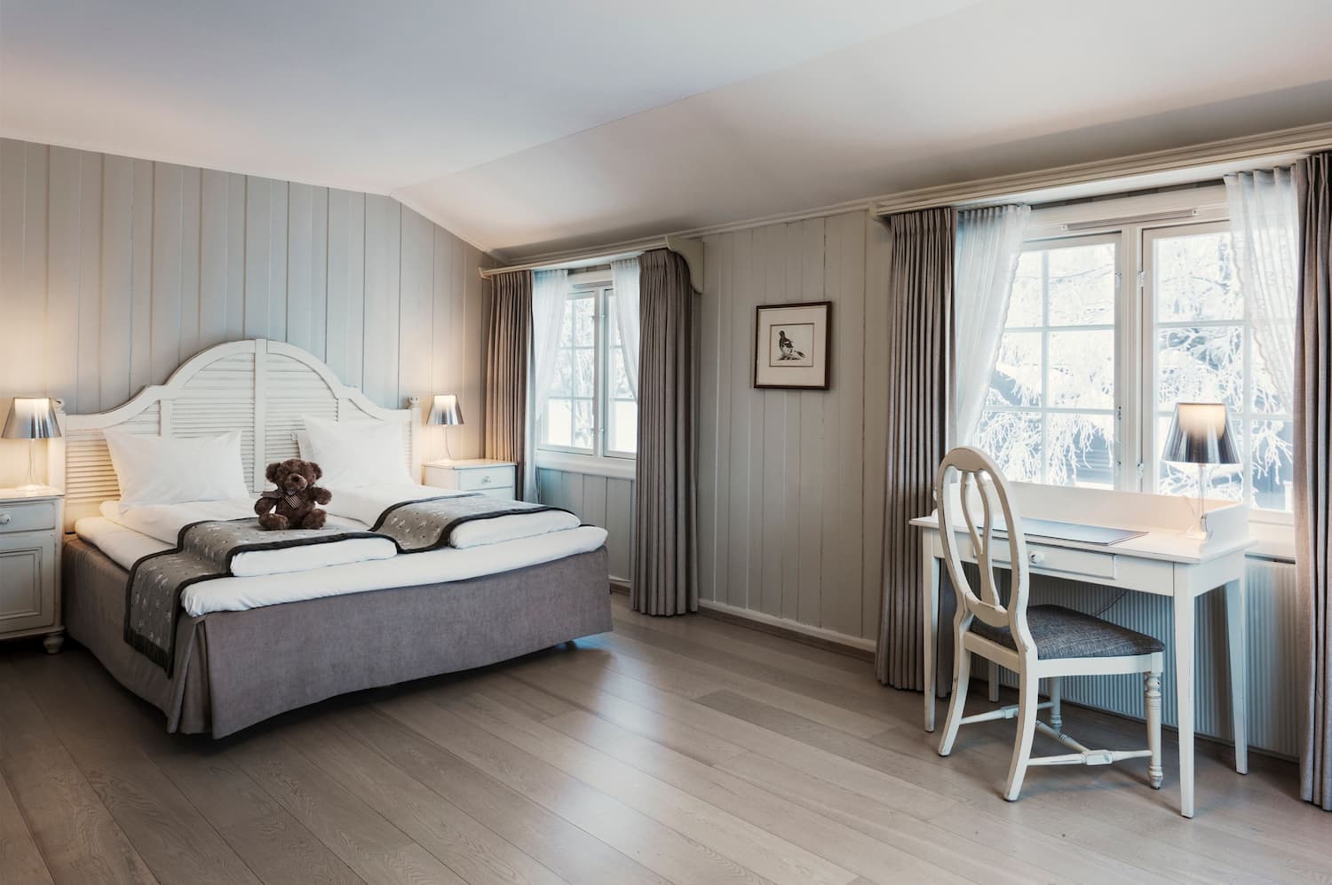 Romslig hotellrom med lyse farger og dobbeltseng med hvit sengegavel. Foto