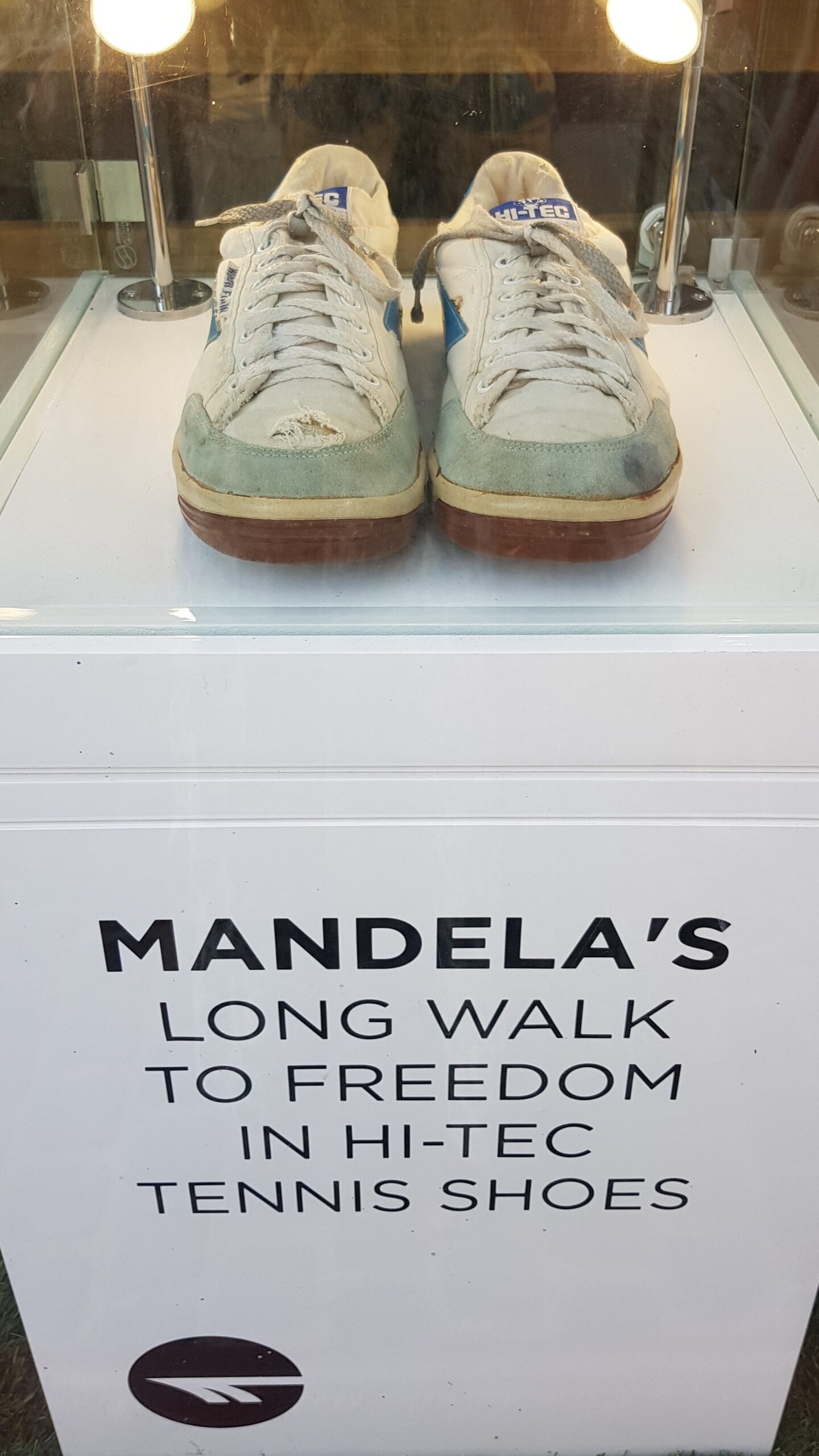 Et par slitte sko på utstilling. Under står det at det er Mandela sine sko. Foto