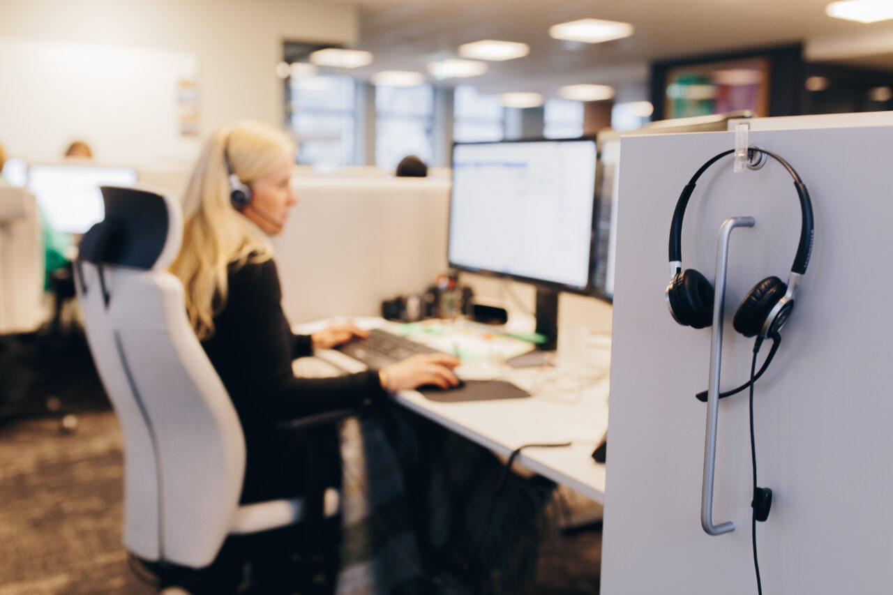 Kvinne sitter foran PC-skjerm med headset på. Foto