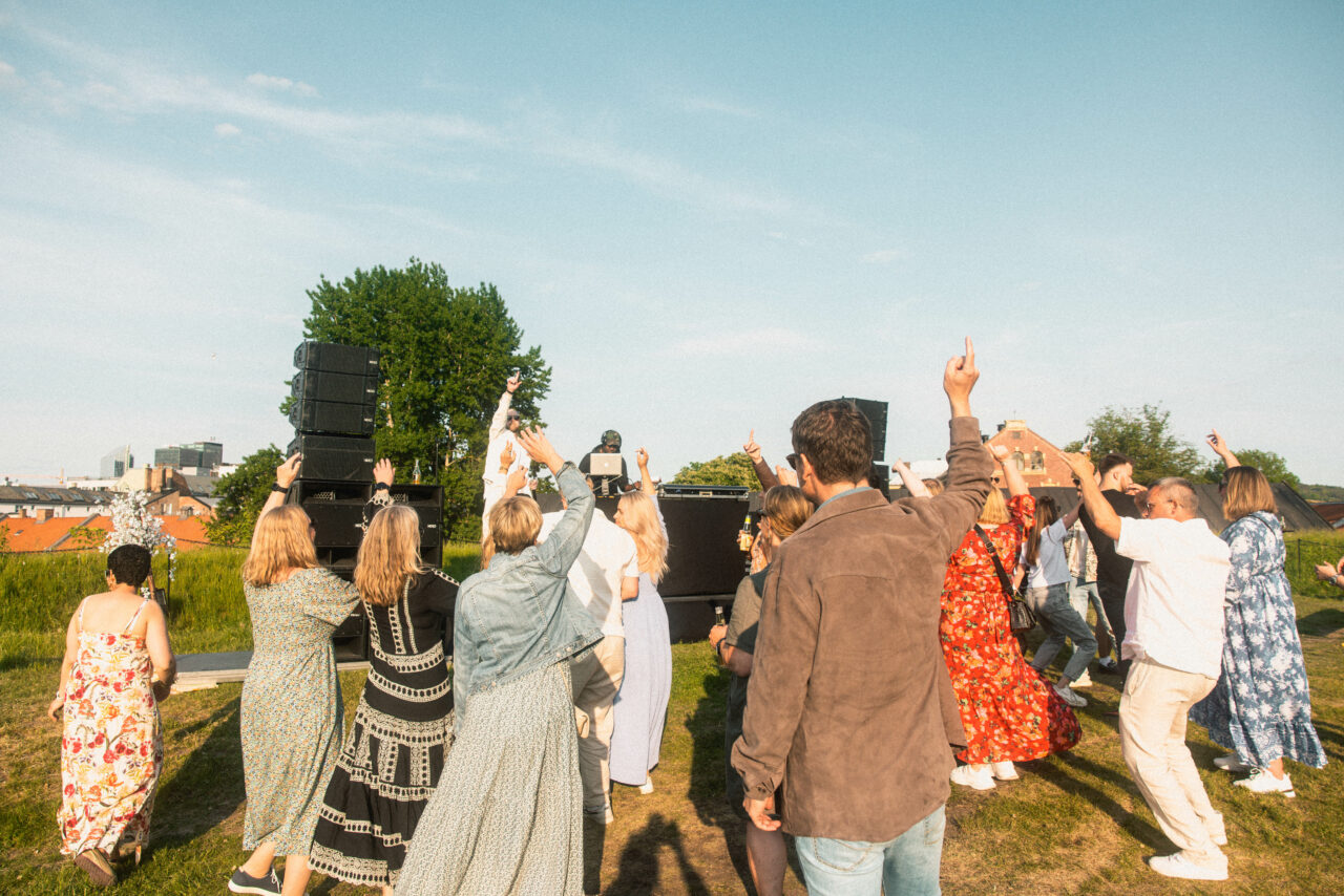 Mennesker står med ryggen mot kamera og danser til en DJ. Foto