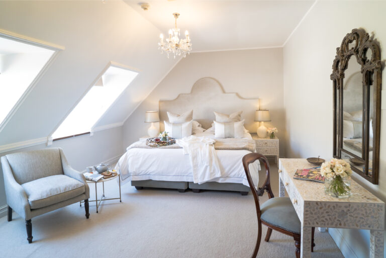 Hvitt stort hotellrom med dobbeltseng og delikat innredning. Foto