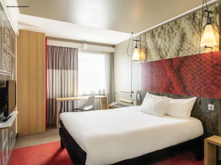 Hotellrom med dobbeltseng i hvitt sengetøy, rødt gulvteppe. Foto