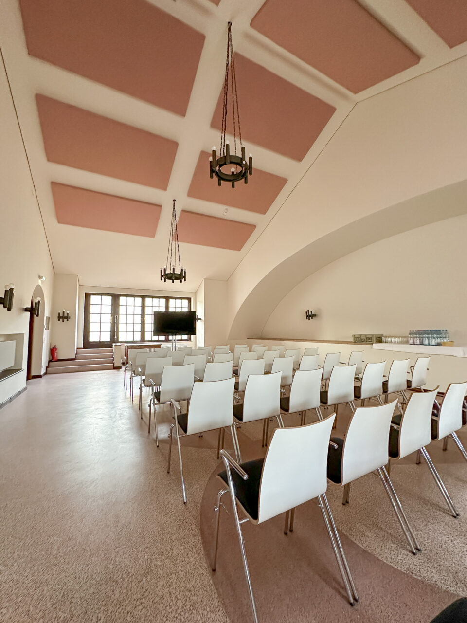 Konferanserom i hvitt med rosa detaljer og stoler i kinoformasjon. Foto