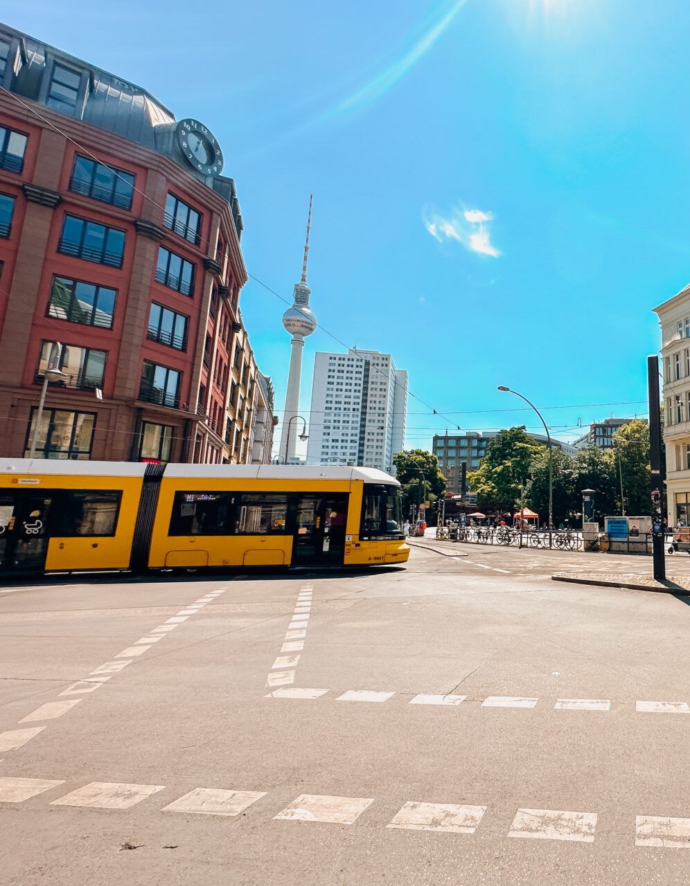 En gul trikk som kjører over et veikryss i Berlin med TV-tårn i bakgrunnen. Foto