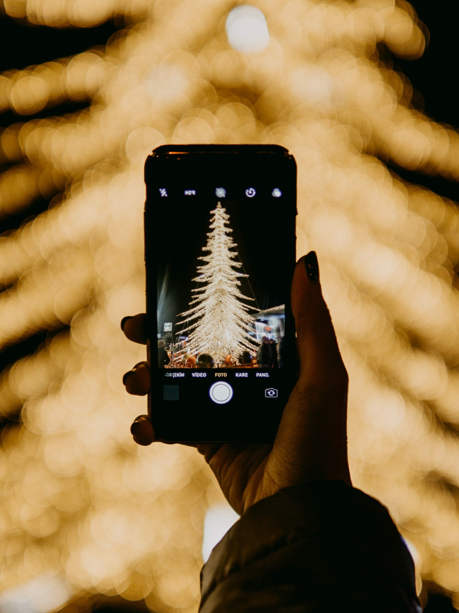 Person holder opp en telefon og tar bilde av et juletre. Foto