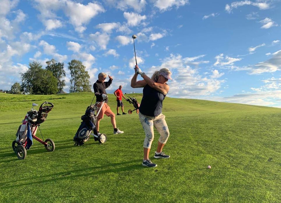 Kvinne står med golfkølle og skal til å slå golfball. Foto