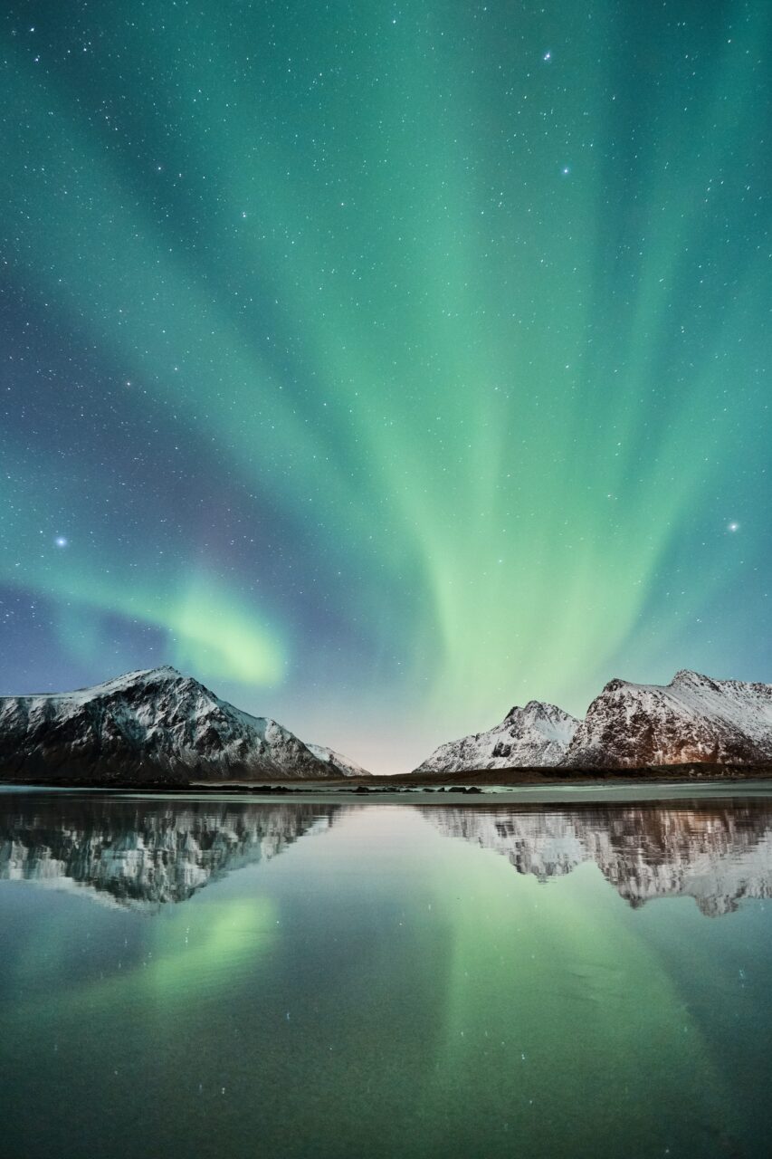 Grønt nordlys som danser over blikkstille vann. Foto